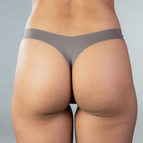 Back view of model wearing Gudia grey seamless thong, seamless design, organic cotton crotch and peach-hip shaping for a smooth, invisible fit under clothing