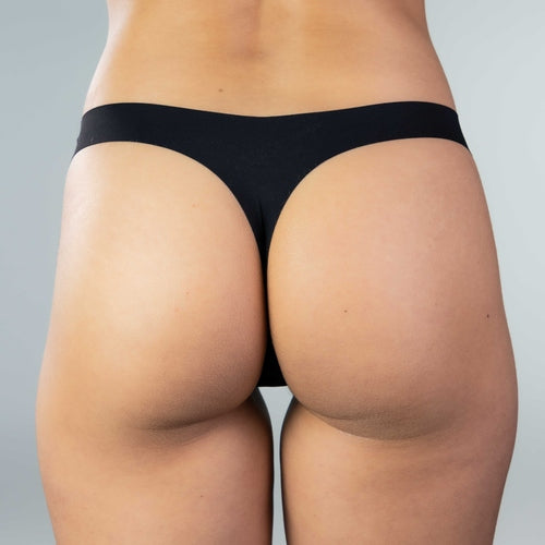Back view of model wearing Gudia black seamless thong, sculpting peach-hip shape and seamless finish with organic cotton crotch for invisible, breathable comfort