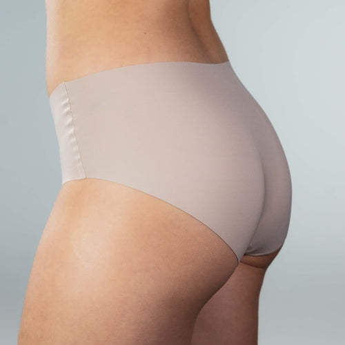 Side-back view of model wearing Gudia sand seamless hipster with mid-rise full coverage fit seamless edges and organic cotton crotch for breathable comfort