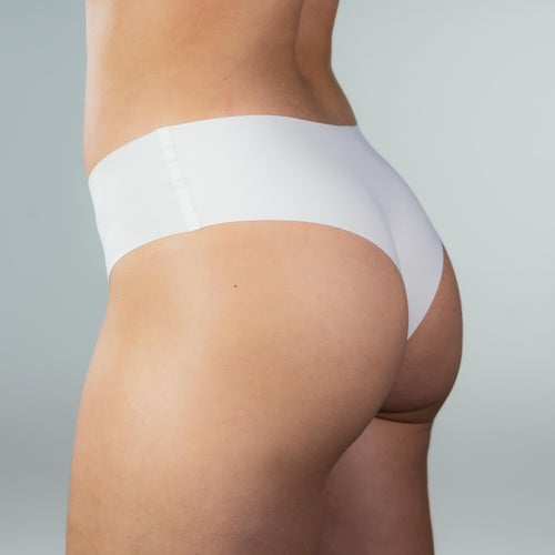 Side back view of model wearing Gudia white seamless Brazilian underwear showing mid-rise fit with sculpted cheeky cut and organic cotton crotch for breathable everyday comfort